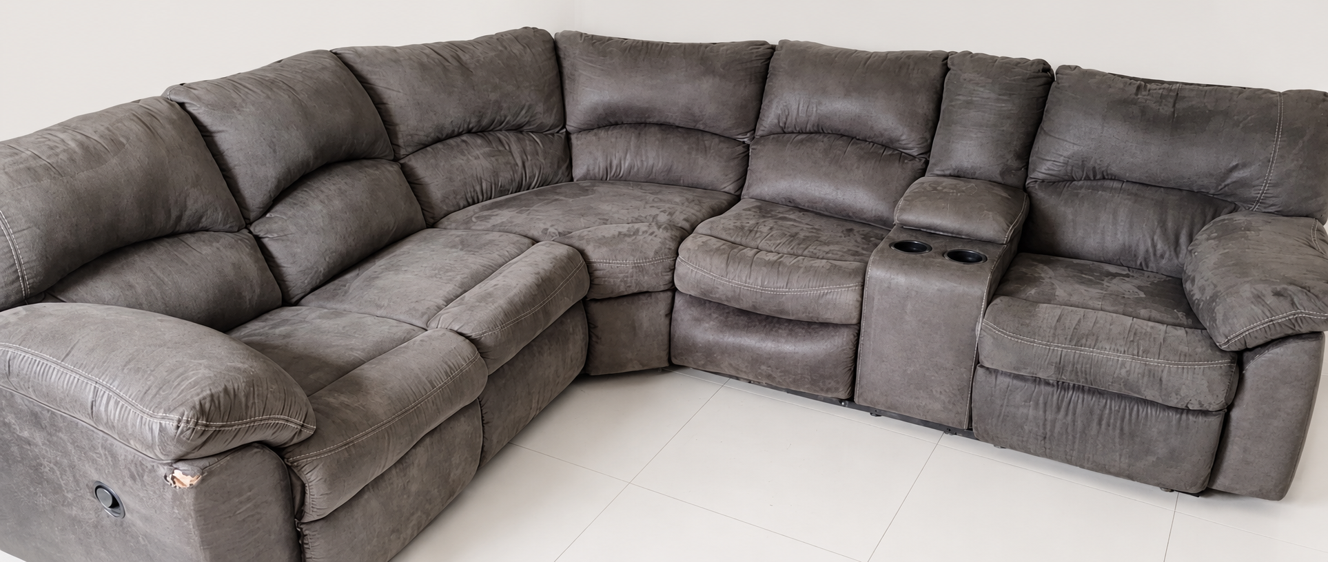 Owner-supplied gray sectional sofa, with visible upholstery wear and a tear on the front-left arm; background cleaned.